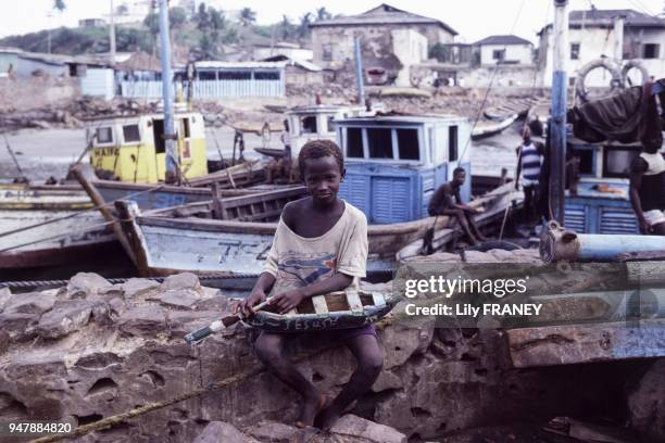 Enfant posant avec sa maquette de bateau en bois au Ghana, en avril 1987.