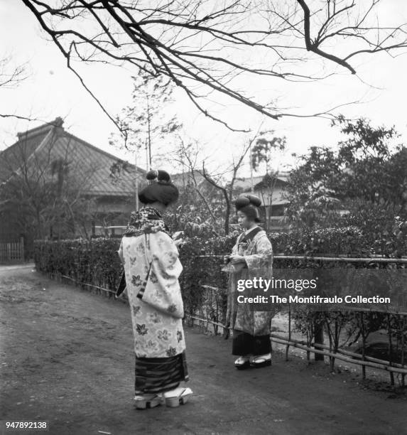 Two Geisha girls, traditional Japanese female entertainers wearing kimonos and Geta footwear, one Geisha girl preparing to take a photograph of the...