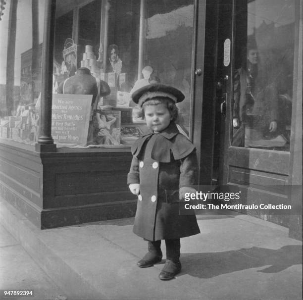 Young boy smartly dressed standing outside a drugstores front door whilst a woman watches him from inside US circa 1900.