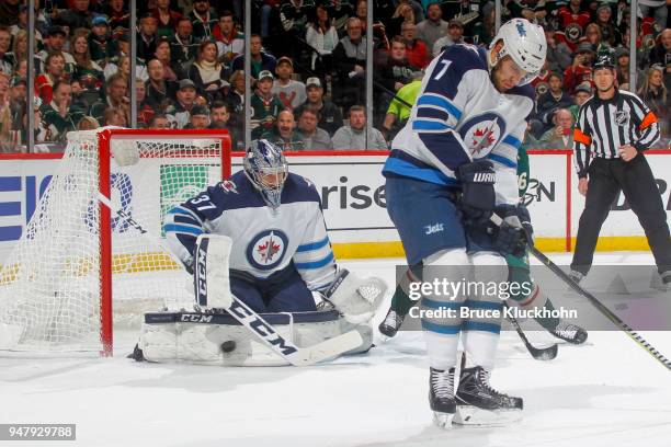 Connor Hellebuyck makes a save while his teammate Ben Chiarot of the Winnipeg Jets defends against the Minnesota Wild in Game Four of the Western...