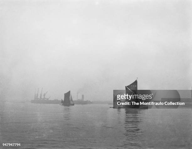 Two Thames barges passing dock cranes on the waters at Sheerness, a town beside the mouth of the River Medway on the north west corner of the Isle of...