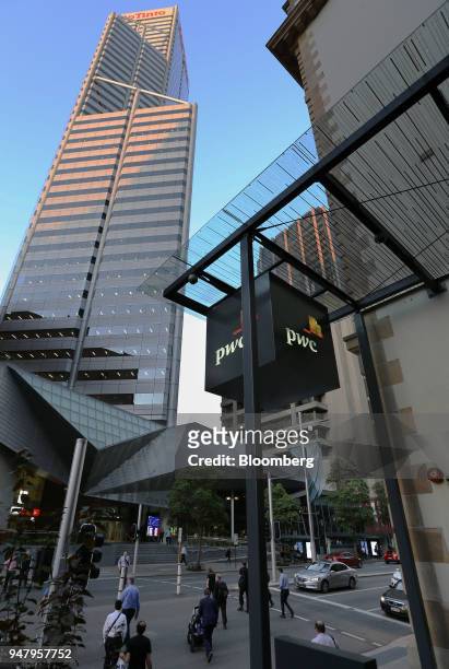 Pedestrians cross an intersection as signage for Pricewaterhouse Coopers International Ltd. Is displayed in the central business district of Perth,...