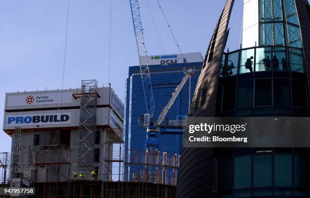 Workers labor at a construction site as people are silhouetted at the observation desk of the Bell Tower, right, in the Elizabeth Quay area of Perth,...