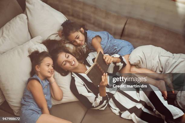mother with daughters reading books in bed - mother daughter couch imagens e fotografias de stock