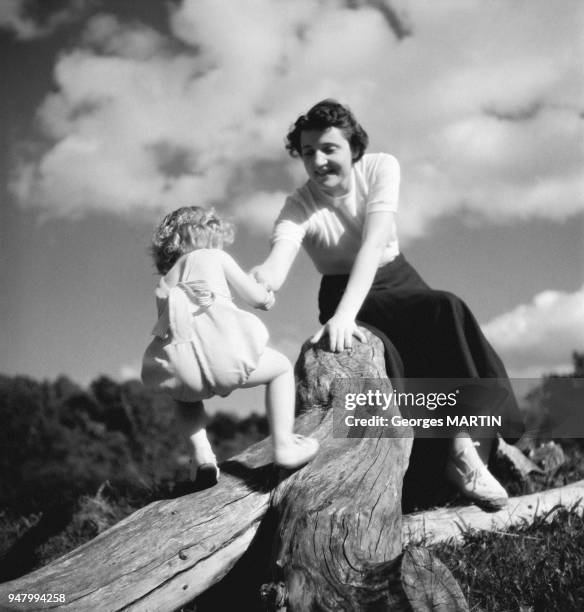 Une mere jouant avec sa fille sur un tronc d'arbre, circa 1960 en France.