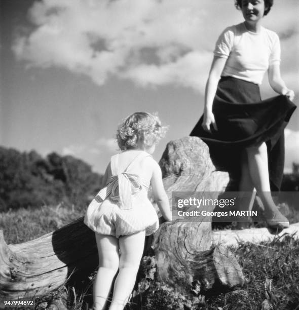 Une mere jouant avec sa fille sur un tronc d'arbre, circa 1960 en France.