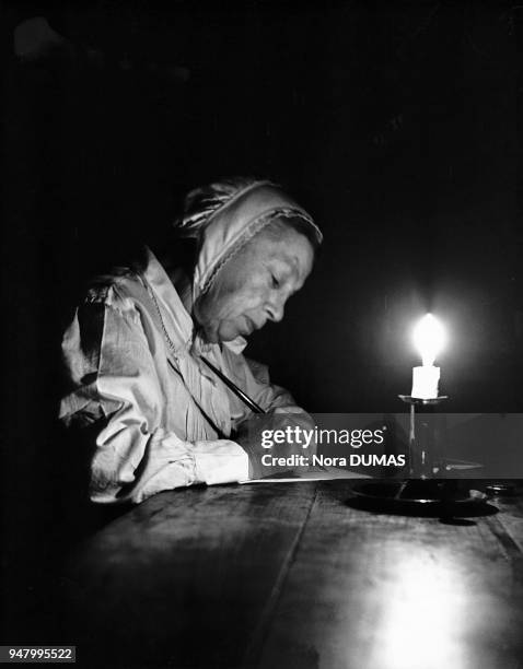 An old lady, in night clothes, is writing by candlelight, 1930. Ile-de-France: Une vieille femme, en tenue de nuit, écrivant à la lueur de la...