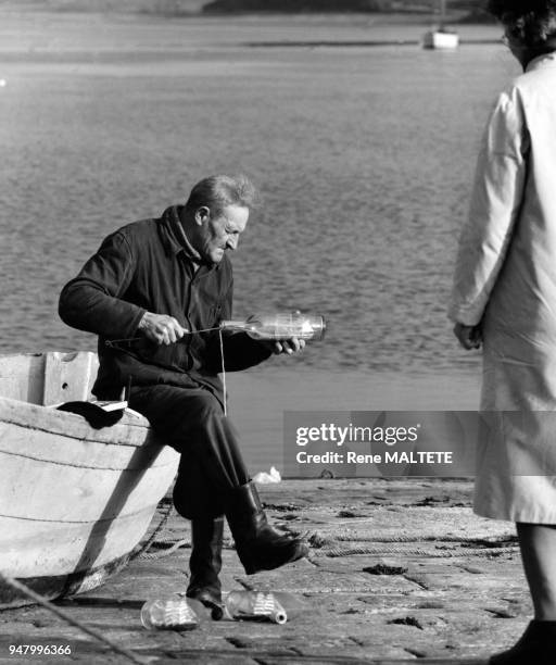 Pêcheur fabriquant des maquettes de bateaux en bouteille, à Plouër-sur-Rance, en décembre 1963, dans les Côtes-d'Armor, France.