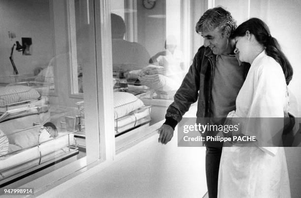 Jeunes parents observant leur bébé dans une maternité, en 1985, France.