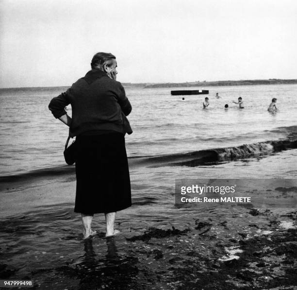 Femme âgée les pieds dans l'eau sur une plage près de Saint-Brieuc, dans les Côtes-d'Armor, en 1960, France.