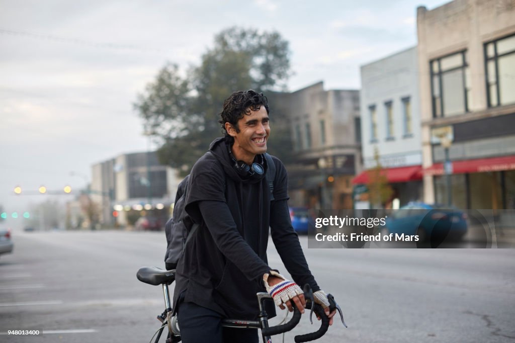 Young Latino man stands smiling with bike in small town square