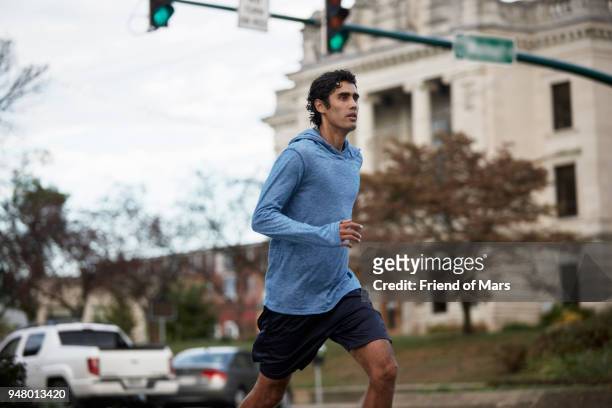 Young Latino man in blue sweatshirt runs by small town courthouse