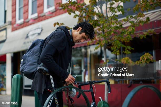 young commuter locks up his bike on bike rack outside - bicycle rack stock pictures, royalty-free photos & images