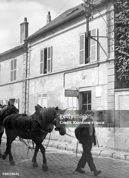Un homme et son cheval passent devant un bureau de poste muni d'une cabine téléphonique publiques en province, circa 1930 en France.