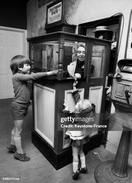 Un petit garçon et sa jeune soeur donnent une pièce de monnaie à leur mère qui tient l'entrée de la salle de jeux depuis une guitoune, circa 1950.