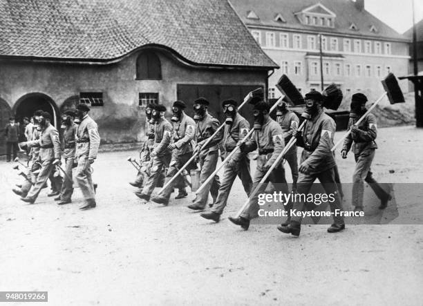 Les employés municipaux, munis de masques à gaz et armés de leurs ustensiles défilent dans les rues d'Allenstein, Prusse-Orientale en juin 1932.