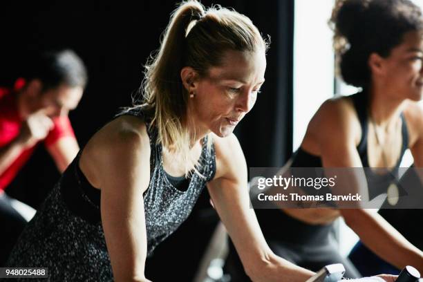 mature woman breathing heavily during indoor cycling class in fitness studio - exercise bike fotografías e imágenes de stock