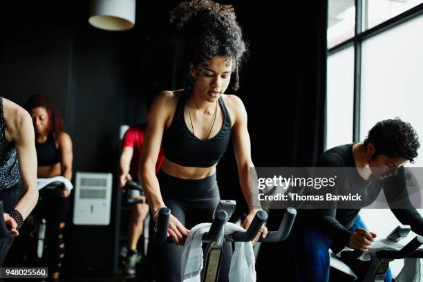 woman riding out of saddle during indoor cycling class in fitness studio - peloton stock pictures, royalty-free photos & images