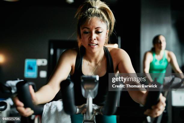 portrait of woman riding indoor bike during class in cycling studio - exercise bike fotografías e imágenes de stock