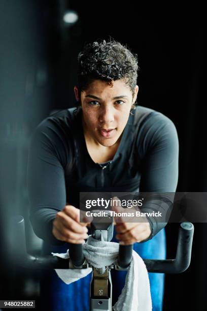 portrait of sweating woman riding indoor bike during cycling class in fitness studio - heimtrainer stock-fotos und bilder