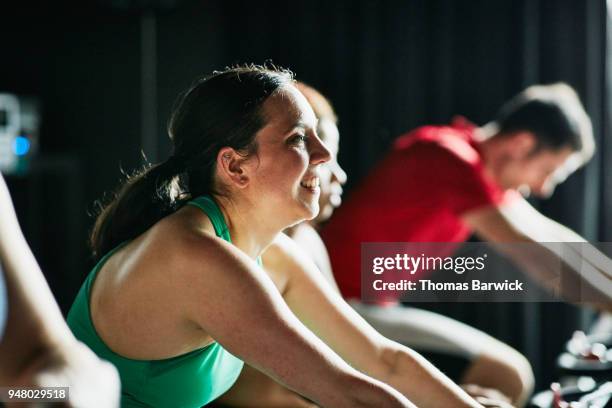 smiling woman riding stationary bike during fitness class with friends in cycling studio - adult male vest exercise stock pictures, royalty-free photos & images