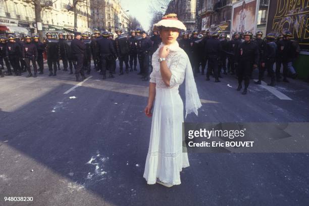Etudiant deguise en jeune femme romantique lors du defile de Mardi Gras avec a l'arriere-plan un mur de policiers le 6 mars 1984 a Paris, France.