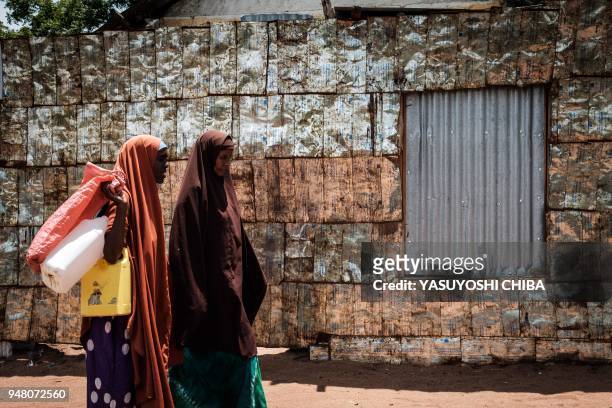 Women walk in front of a metal fence made of vegetable oil cans from USAID at the Dadaab refugee complex, northeastern Kenya, on April 18, 2018. -...