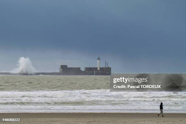 Dans la rade de Boulogne Sur Mer, les vagues se déchainent sur le mur de protection et le vent fait voler le sable sur la plage.