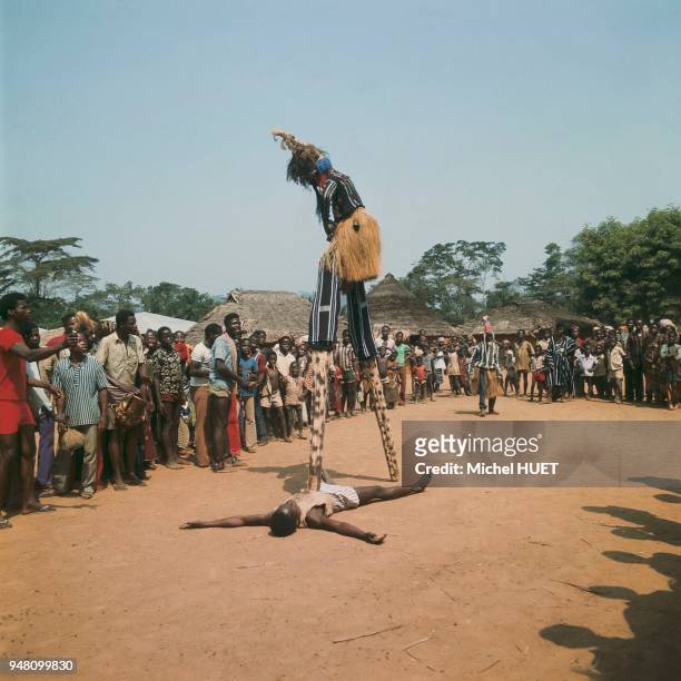 Un danseur yacouba porte le masque à échasses Gle gben en Côte d'Ivoire vers 1950-1960. Le danseur porte une cagoule en filet noir, une haute...