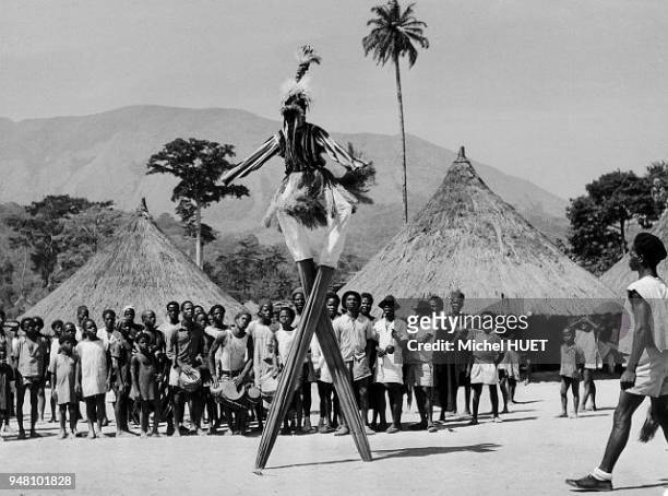 Un danseur yacouba porte le masque à échasses Gle gben en Côte d'Ivoire vers 1950-1960. Le danseur porte une cagoule en filet noir, une haute...