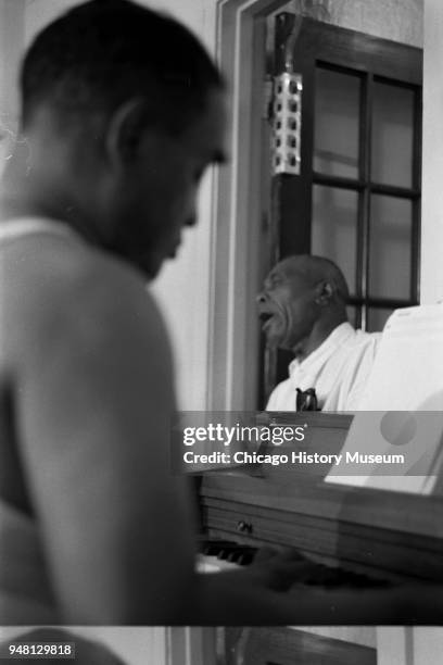In his home, Little Brother Montgomery plays piano as Sunnyland Slim sings in the background, Chicago, Illinois, circa August 1968.