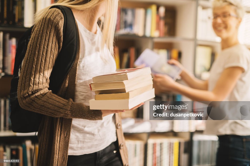 Close view of book stack held by a young high school student girl in the library.