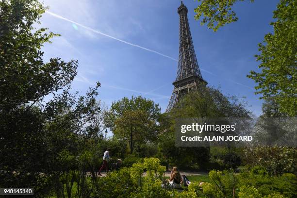 People enjoy the warm weather and the sun below the Eiffel Tower on the Champ-de-Mars park on April 18, 2018 in Paris.