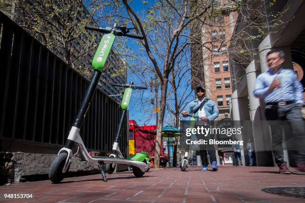 Pedestrians walk past Neutron Holdings Inc. LimeBike shared electric scooters parked in San Francisco, California, U.S., on Friday, April 13, 2018....