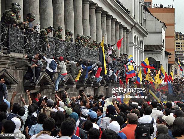 Crowd of Ecuadorians wave flags and shout encouragement to those attempting to climb up to armed troops guarding the presidential palace in Quito...