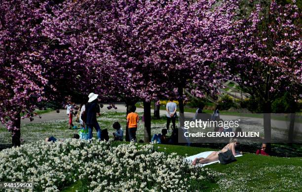 People enjoy a sun bath at the Parc Floral of the Bois de Vincennes in Paris on April 18, 2018.
