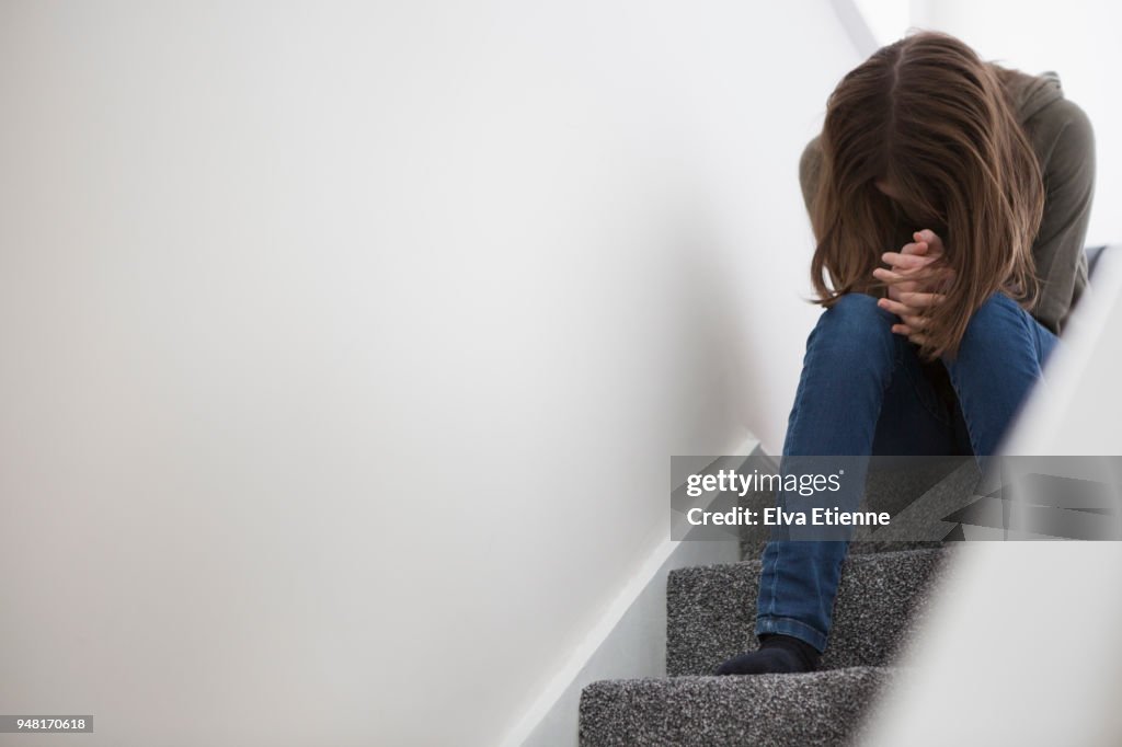 Teenage girl sitting on stairs with head down in despair