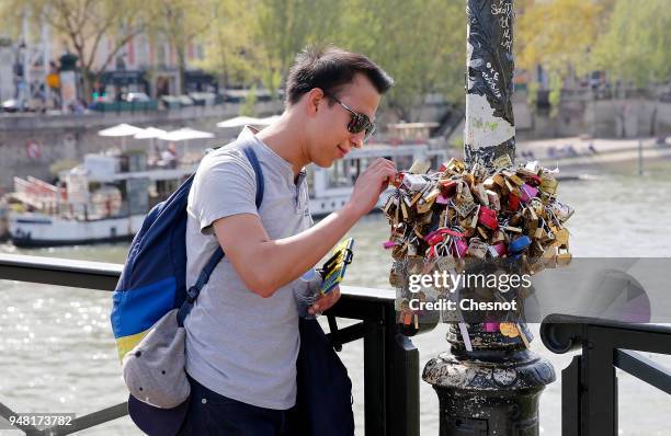 An asian tourist hangs a padlock of love at a street lamp on the "Pont des Arts" on April 18, 2018 in Paris, France. Paris city hall has replaced the...