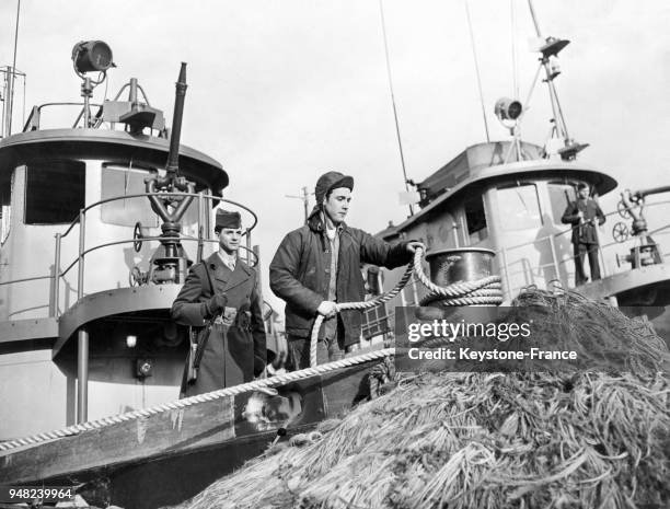 Un pêcheur enroule l'aussière d'un navire pour son amarrage sous la surveillance d'un garde armé dans le port de New York, Etats-Unis en 1946.