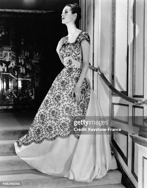 Mannequin présentant un modèle Hattie Carnegie de la Collection Printemps 1956: une robe de bal en organza rose pâle brodée de noir avec des bijoux...