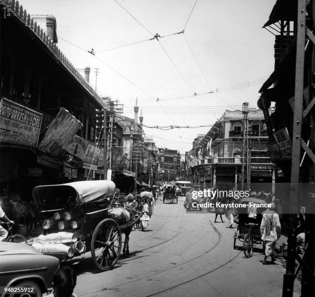 Circulation où se mèlent charettes, cyclo-pousse, chariots et voiture moderne dans une rue commerçante de Delhi, Inde, circa 1950.