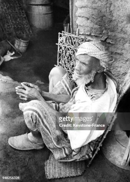 Un vieil homme assis dans la rue près de son échoppe dans le souk des artisans en juillet 1936 à Marrakech, Maroc.