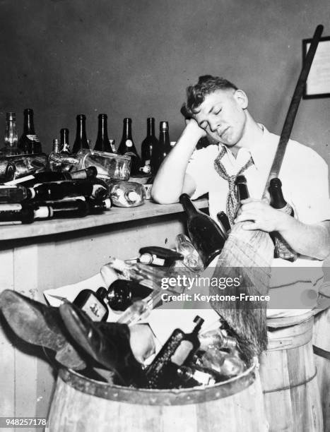 Un garçon d'un bar affalé sur une chaise et les pieds dans une poubelle remplie de bouteilles vides après avoir célébré la fin de la prohibition, à...