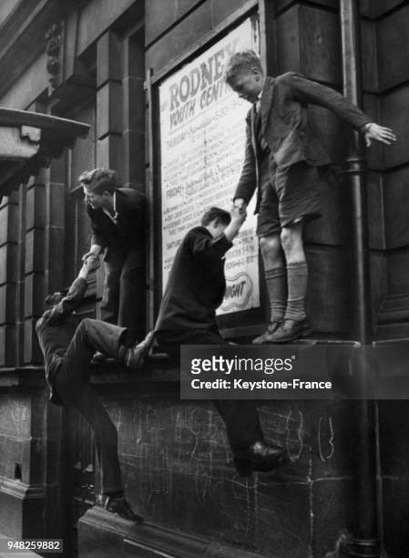 Quatre jeunes garçons se perchent sur le rebord d'un immeuble devant l'entrée du Rodney Youth Centre en attendant qu'il ouvre, circa 1940 à...