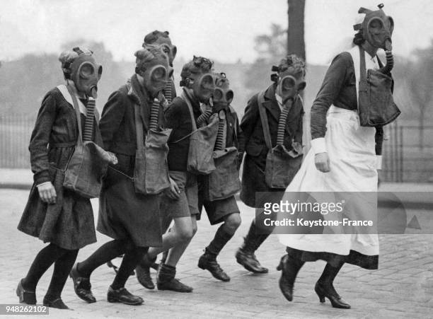 Des enfants munis de masques à gaz suivent une infirmière dans les rues de Londres, Royaume-Uni circa 1930.