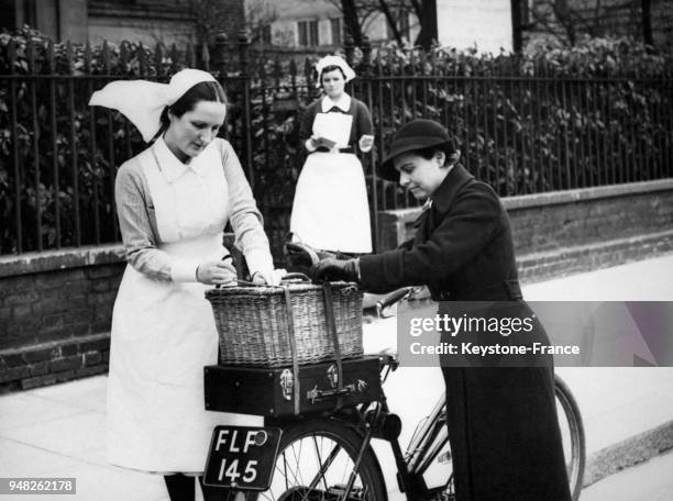 Une sage-femme avec l'aide d'une infirmière met le nécessaire médical et des analgésiques dans le panier de sa bicyclette avant de se rendre chez une...