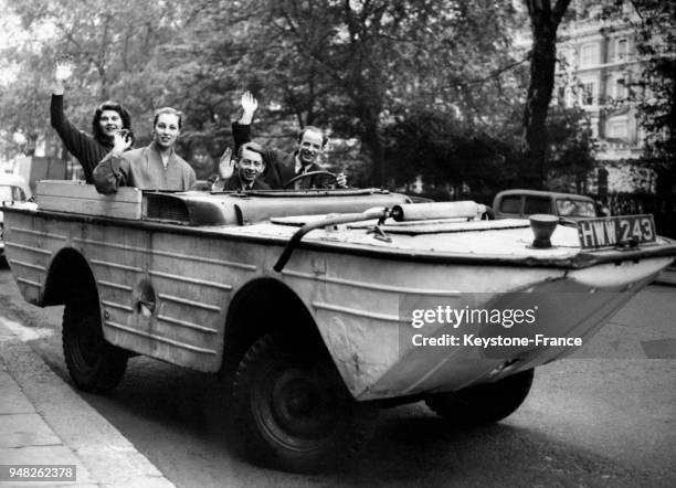 Deux jeunes femmes et deux jeunes hommes saluent depuis leur Jeep amphibie à bord de laquelle ils vont entreprendre un voyage jusqu'en Australie,...