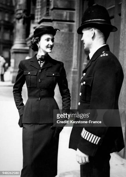 Femme vêtue de l'ensemble jupe-veste de la nouvelle collection de Charles Creed, pose à côté d'un policier en uniforme, à Londres, Royaume-Uni en...