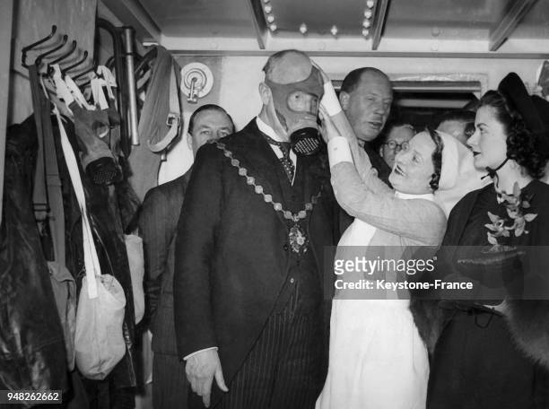 Une infirmière met au maire de Westminster un masque à gaz lors de sa visite dans le premier abri anti-aérien, à ses côtés l'actrice Margaret...