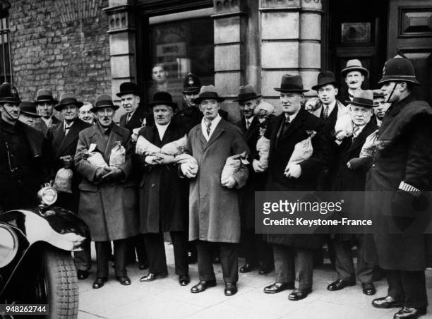 Des policiers encadrent les membres du PSA Slate Club qui sortent du club avec leurs gains partagés gagnés lors des paris le 9 décembre 1933 à...